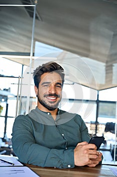 Happy Latin business man using mobile phone in office, vertical portrait.
