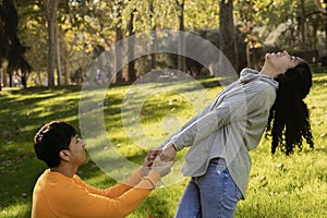 Happy latin couple enjoy time together on a public park. Boyfriend holding girlfriend hands asking for marriage