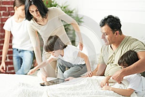 Happy latin family with cute little kids using tablet pc in the morning. Loving parents playing together with children