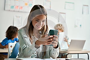 Happy latin hispanic kid girl school student using smartphone in classroom.