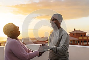 Happy Latin senior couple having romantic moment dancing on rooftop during sunset