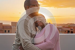 Happy Latin senior couple having romantic moment embracing on rooftop during sunset time