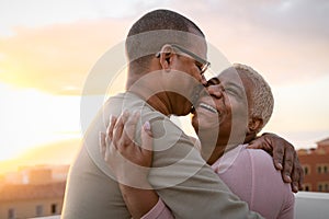 Happy Latin senior couple having romantic moment embracing on rooftop during sunset time