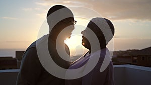 Happy Latin senior couple having romantic moment kissing on rooftop during sunset