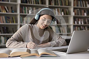 Happy Latin student girl in wireless earphones studying in library