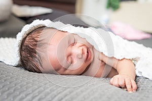 Happy Latina baby sleeping smiling on a bed covered with a white blanket