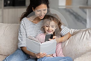 Happy Latino mom and daughter read book use cell