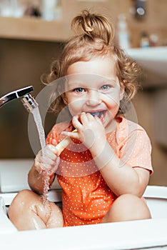 Happy laughing baby girl brushing her teeth in the bath