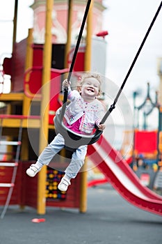 Happy laughing baby girl in a swing on a playground