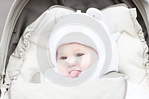 Happy laughing baby in a warm hat sitting in a stroller