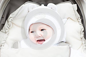 Happy laughing baby in a warm hat sitting in a stroller