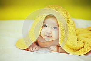 Happy laughing baby wearing yellow hooded towel lies on parents bed after bath or shower . newborn holds its head. Beautiful baby