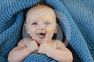 A happy laughing baby wrapped in a cosy bllue blanket