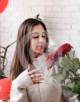 Happy laughing beautiful woman sitting in the bed celebrating valentine day holding red roses