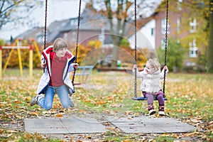 Happy laughing boy and baby sister playing on swing