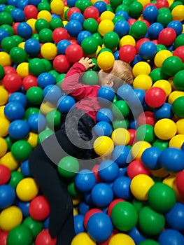 Happy laughing boy having fun in ball pit on birthday party in kids amusement park and indoor play center