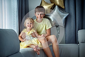Happy laughing boy and his baby sister pose on sofa