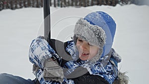 Happy laughing boy riding on zipline at public playground covered with snow after blizzard. Fun and joy on winter holidays.