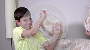 Happy laughing brother and sister having a pillow fight in sofa at home