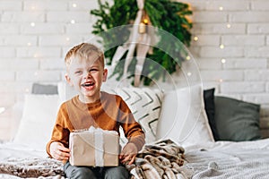 Happy laughing Caucasian boy with his presents on Christmas morning. Christmas tree wreath on background. Child excited