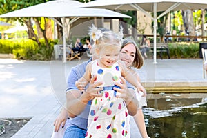 Happy laughing child girl in white dress in colored peas with her parents having fun near pond, lake in the park. Family recreatio