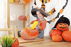 Happy laughing child girl in a witches hat cut a pumpkin for Hal