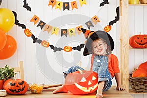 Happy laughing child girl in a witches hat cut a pumpkin for Hal