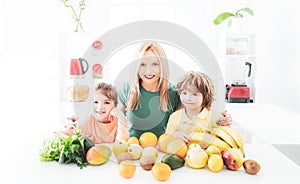 Happy laughing children and her beautiful young mother making fresh strawberry and other fruit juice in kitchen. Happy
