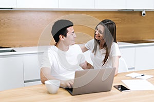 Happy laughing couple is together using laptop and looking at each other at home