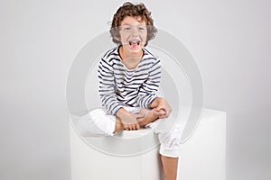 Happy laughing curly boy sitting over white background. Fashion