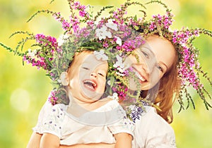 Happy laughing daughter hugging mother in wreaths of summer flowers