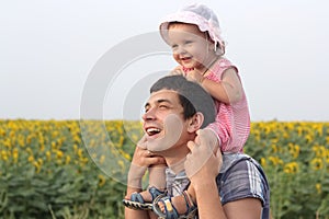 Happy laughing father holding baby daughter on daddy's shoulders standing together in sunflowers meadow enjoying