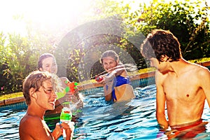 Happy laughing friends play water-gun in pool