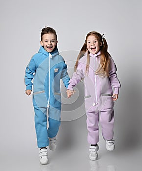Happy laughing, frolic kids boy and girl in blue and pink jumpsuits with hoods and pockets are running together