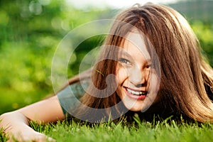 Happy laughing fun casual kid girl lying on the grass on nature spring green background. Closeup