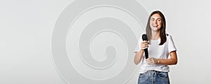 Happy laughing girl holding microphone and singing karaoke, white background