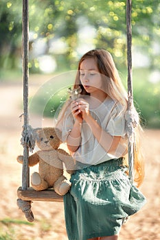 Happy laughing kid girl with long hair enjoying a swing ride on a sunny summer day