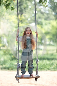 Happy laughing kid girl with long hair enjoying a swing ride on a sunny summer day