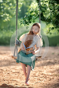 Happy laughing kid girl with long hair enjoying a swing ride on a sunny summer day