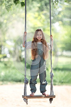 Happy laughing kid girl with long hair enjoying a swing ride on a sunny summer day