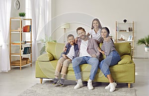 Happy laughing kids boy and girl having fun with their parents, sitting on sofa at home.