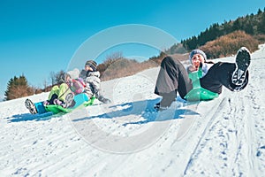 Happy laughing kids sliding down from the snow slope riding sleighs. Funny winter holidays spending concept image