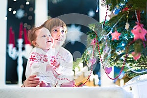 Happy laughing kids under a beautiful Christmas tree in a dark living room