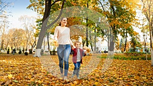 Happy laughing little boy walking his mother on yellow fallen leaves at autumn park