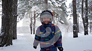 Happy laughing little child runs towards the camera among the trees in a snowy forest or park. Recreation, sports and