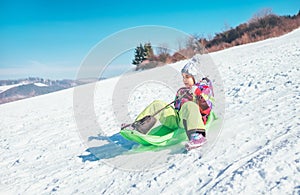 Happy laughing little girl sliding down from the snow slope. Funny winter holidays spending concept image