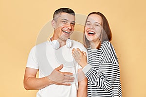 Happy laughing man and woman wearing casual clothing standing isolated over beige background expressing positive emotions being in