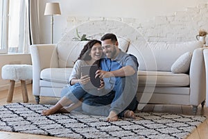 Happy laughing married couple using tablet, sharing digital device