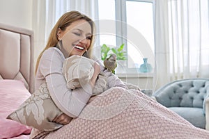 Happy laughing mature woman and green parrot at home in bed