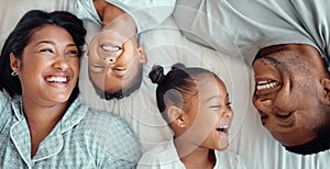 Happy laughing mixed race family with two children relaxing and lying together on a bed at home, from above. Faces of